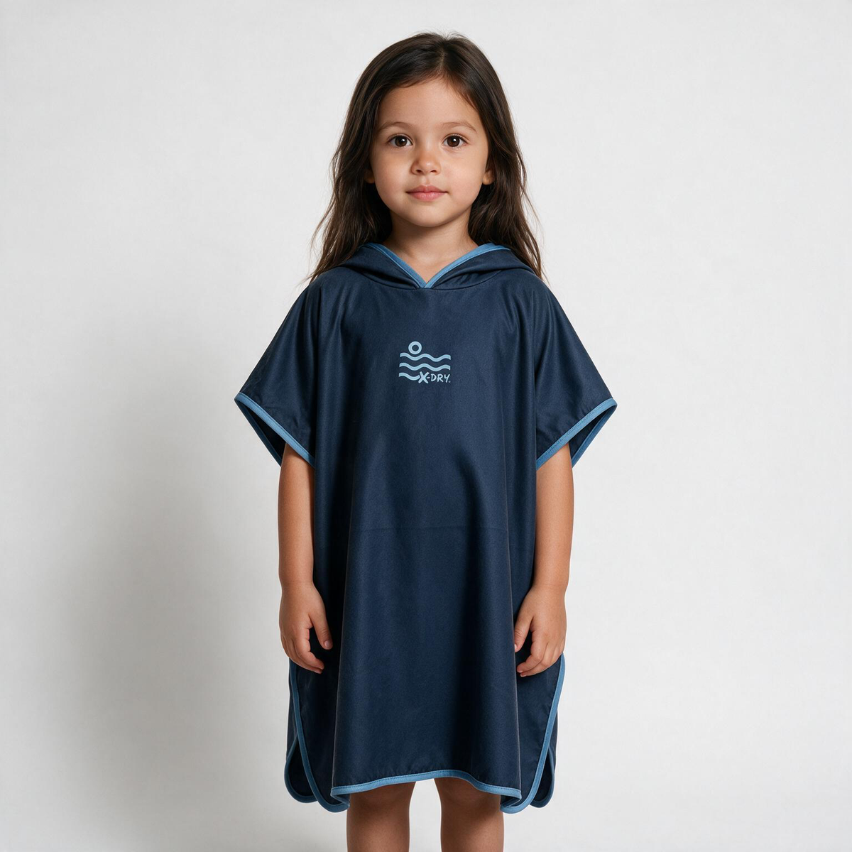 A young girl stands against a light gray studio background wearing a navy blue hooded poncho with light blue trim and a white 'Piscis' logo on the chest.