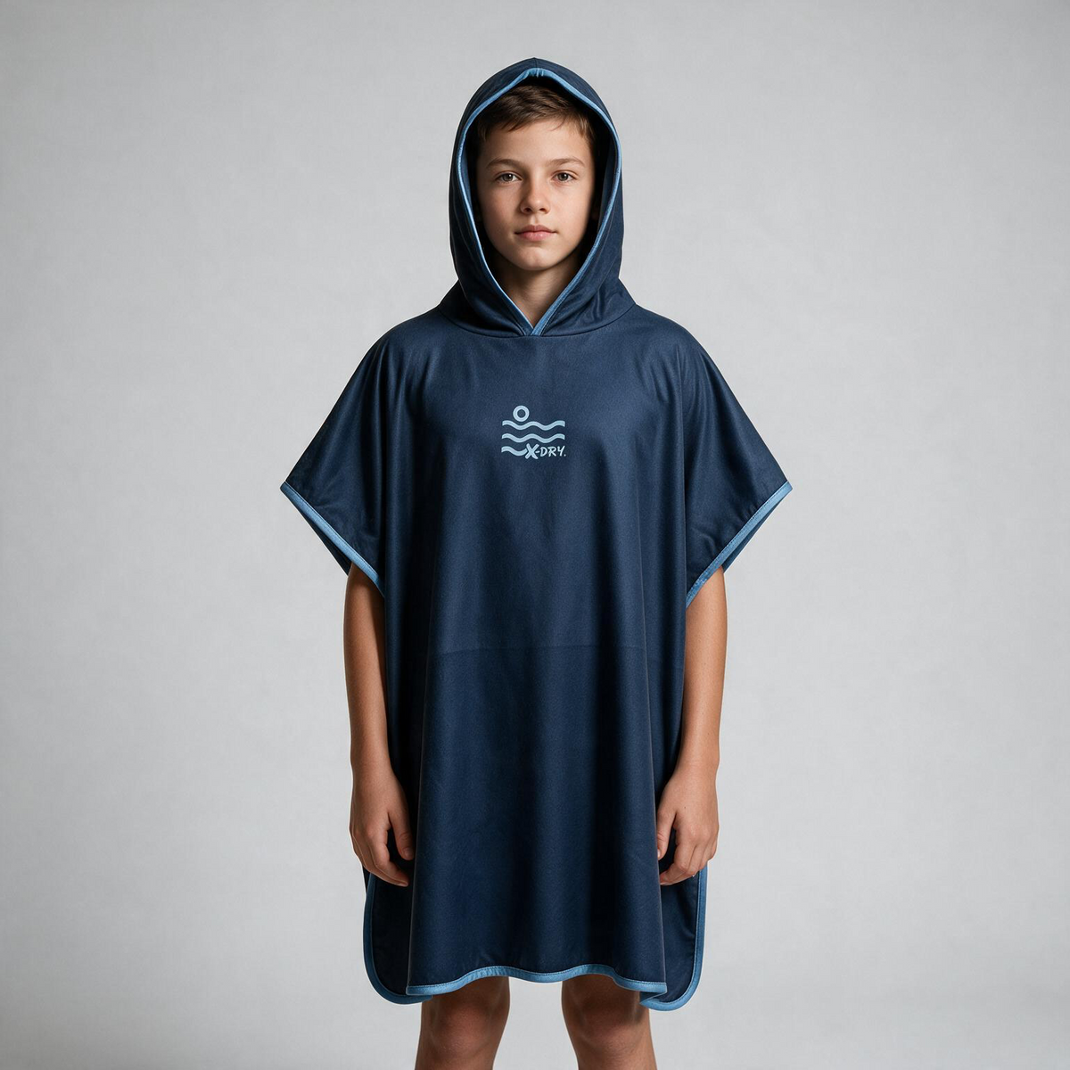 A child wearing a navy blue hooded poncho with light blue trim and a white logo on the chest, standing against a light gray studio background.
