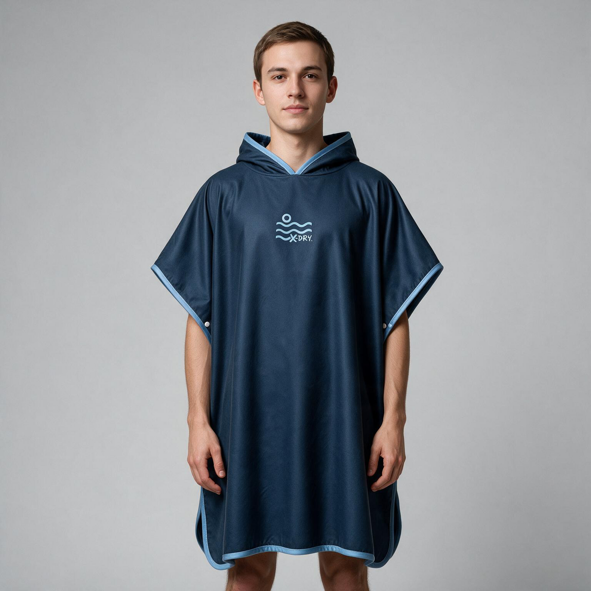 A man wearing a dark blue hooded poncho-style rain suit with light blue trim and a white logo on the chest, standing against a plain light gray studio background.
